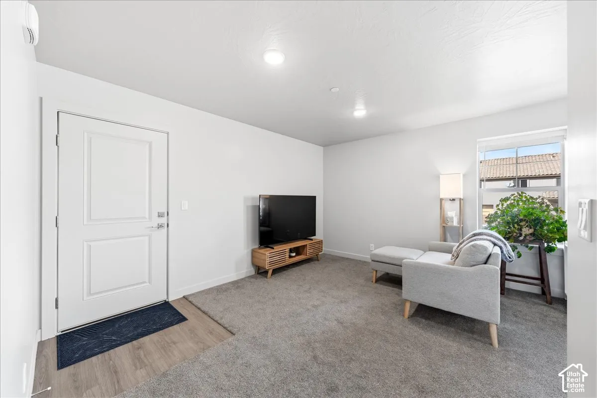 Recessed lighting illuminates the living space with grey carpeting and a two-panel entry door