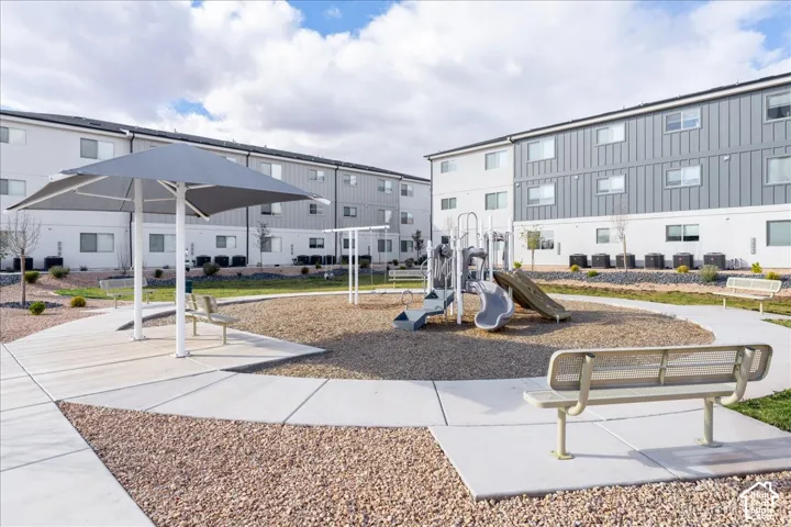 Outdoor playground with slide and climbing structure, shaded seating area, and surrounding paved walkways