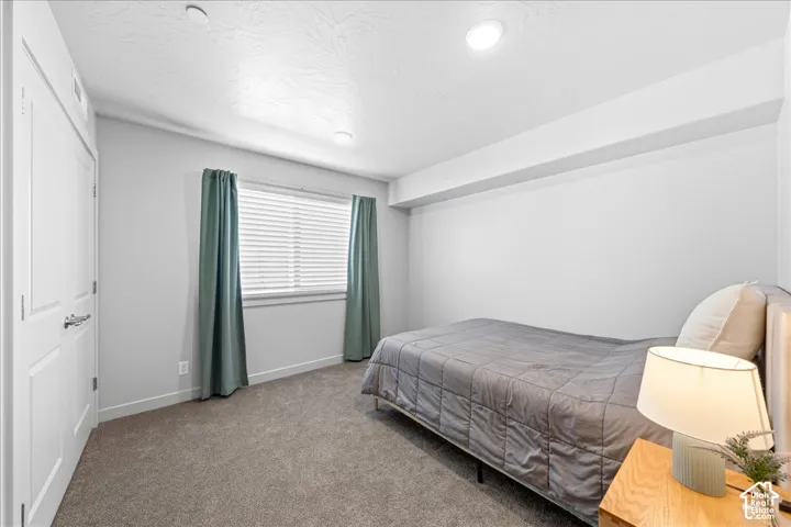 Bright secondary bedroom featuring neutral carpeting, recessed ceiling lighting, and large window with green thermal curtains and horizontal blinds