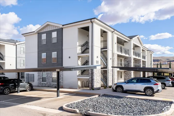 Modern apartment building with a white stucco facade, dark grey siding accents, stone veneer on the lower level, and covered parking structures