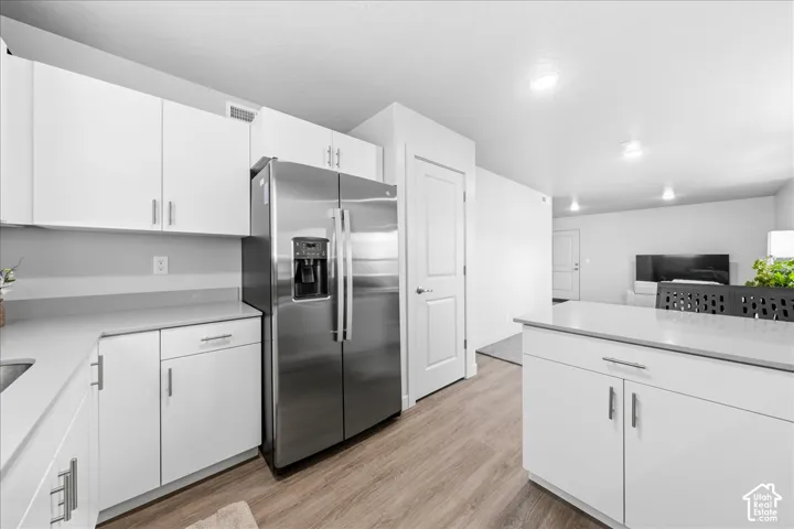 Kitchen featuring white cabinetry, light-toned countertops, a stainless steel refrigerator, and wood-finish flooring