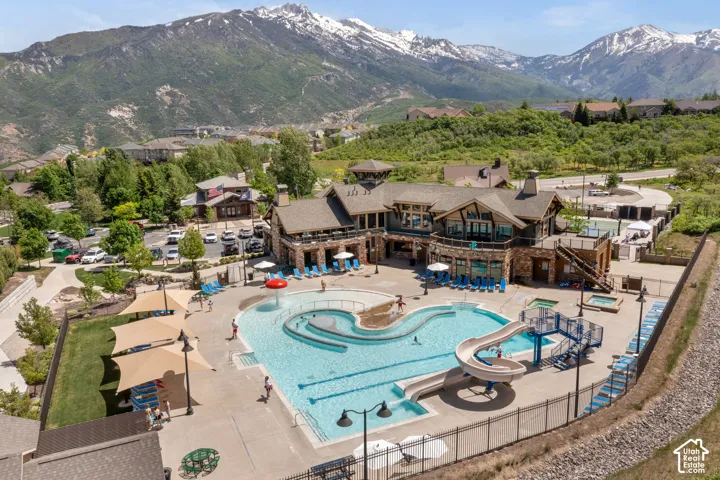 Outdoor swimming pool with water slide, separate children's splash area, multiple shade structures, and hot tubs