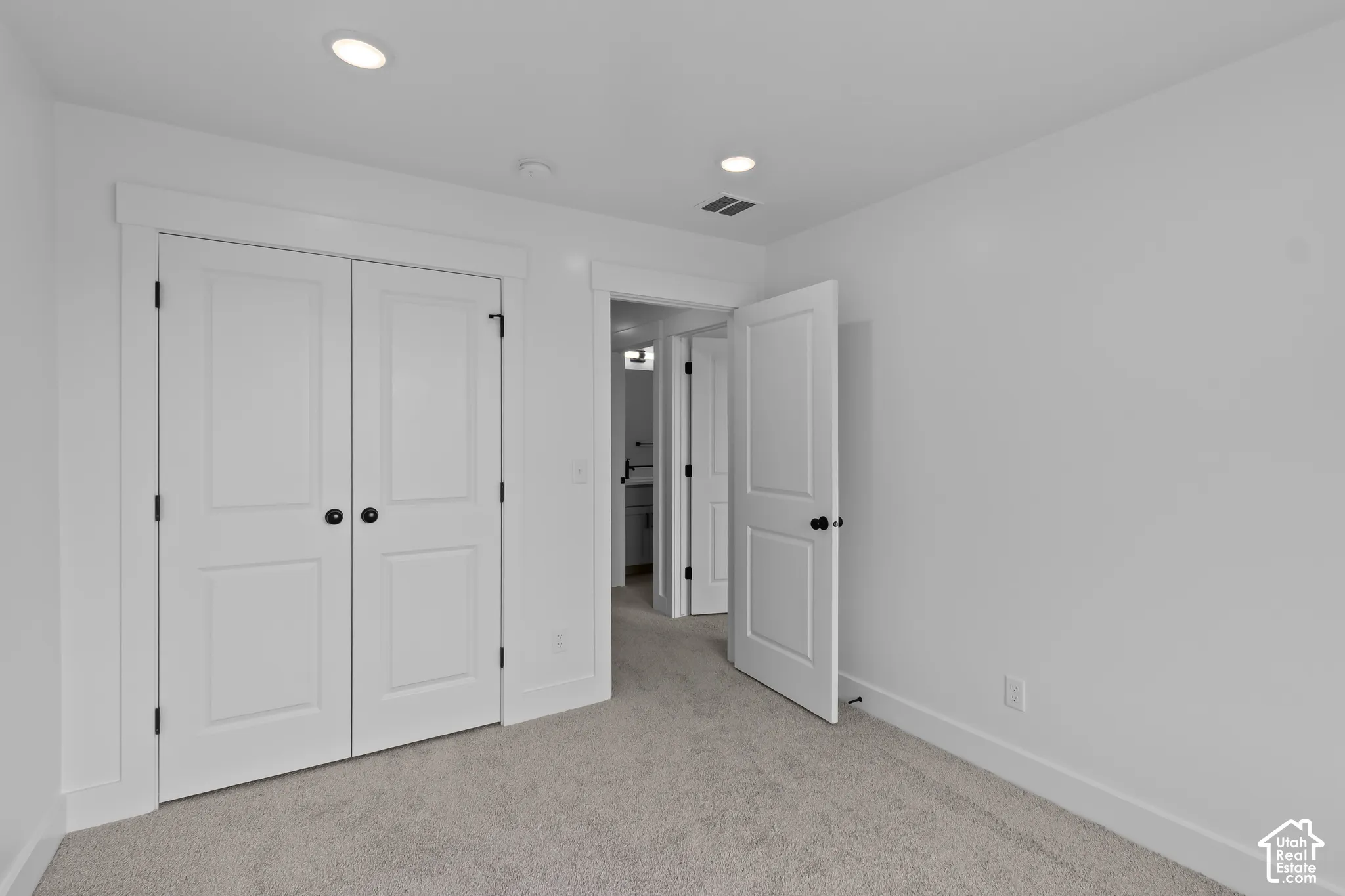 Recessed ceiling lighting, white interior doors with matte black hardware, light-toned carpeting, and crisp white wall finishes