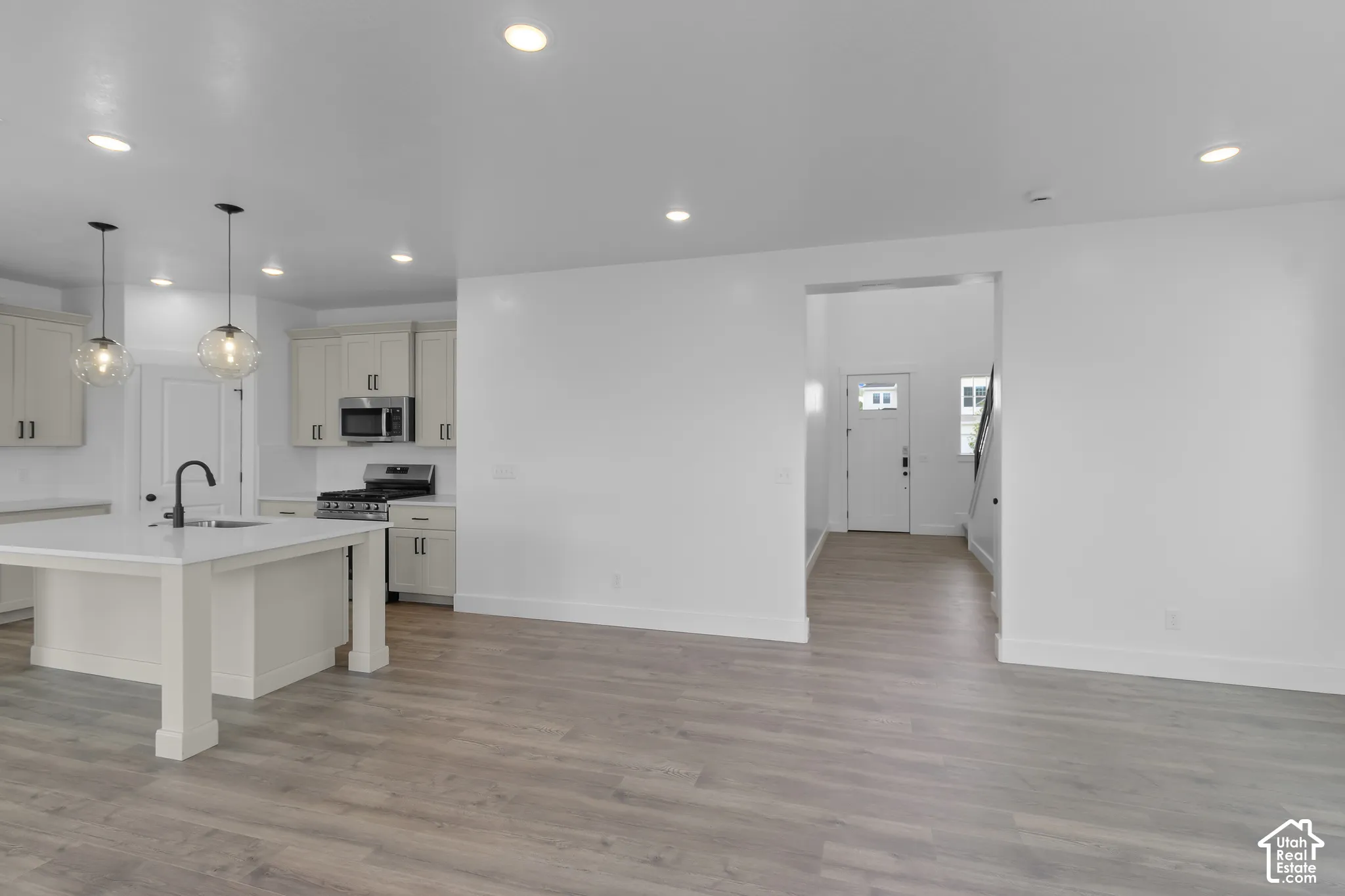 Open-concept living area featuring wood-finish flooring, recessed lighting, a kitchen island with pendant lighting, light-toned cabinetry, and stainless steel appliances