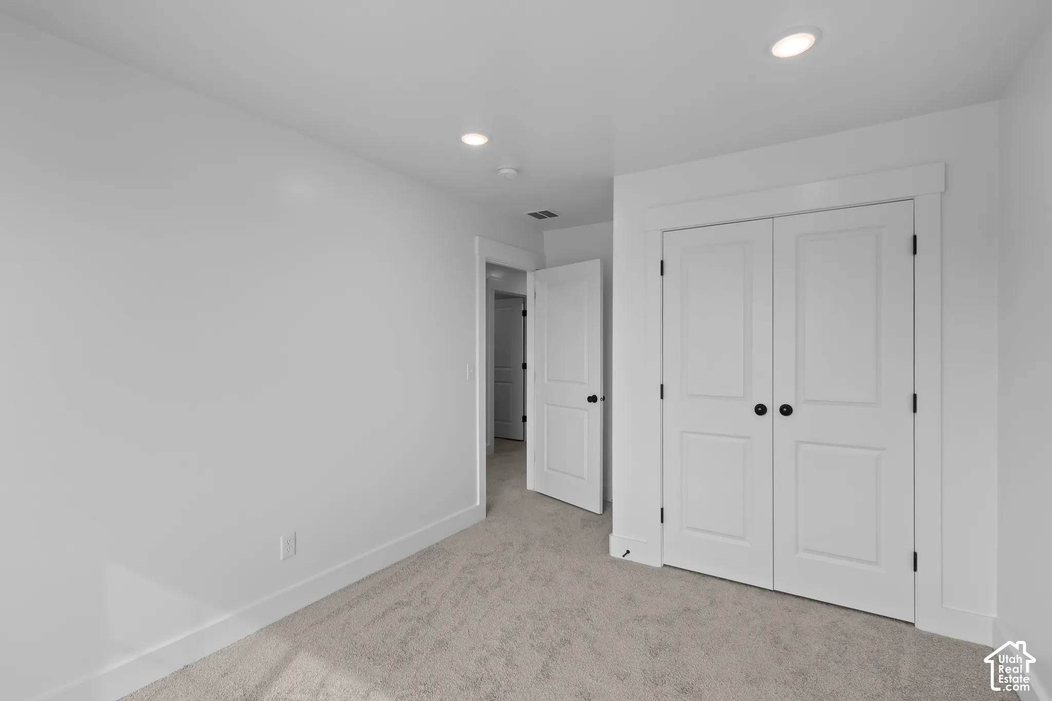 Recessed lighting, white trim, paneled doors with black hardware, and neutral carpeting