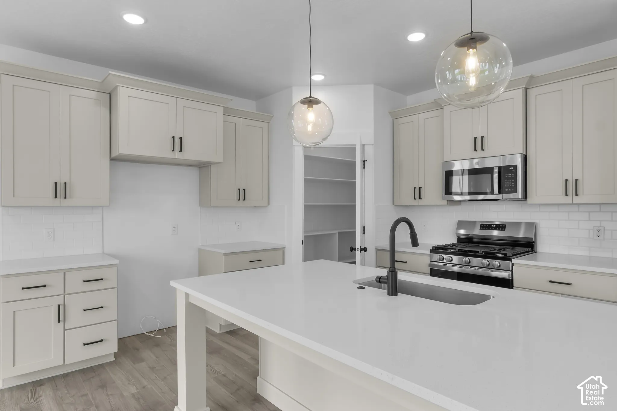 Kitchen featuring light-toned cabinetry, stainless steel appliances, a center island with an undermount sink, and wood-finish flooring