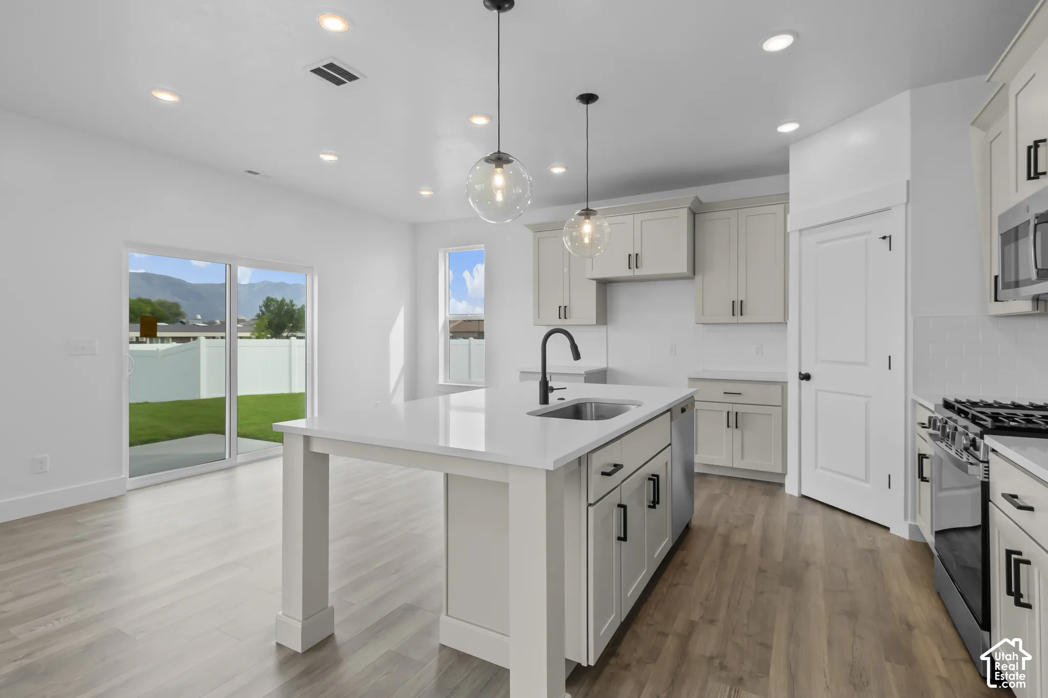 Kitchen featuring an island with a built-in sink, stainless steel appliances, light-toned cabinetry, and mixed wood-finish flooring