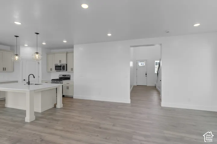 Open-concept living area featuring wood-finish flooring, recessed lighting, a kitchen island with pendant lighting, light-toned cabinetry, and stainless steel appliances
