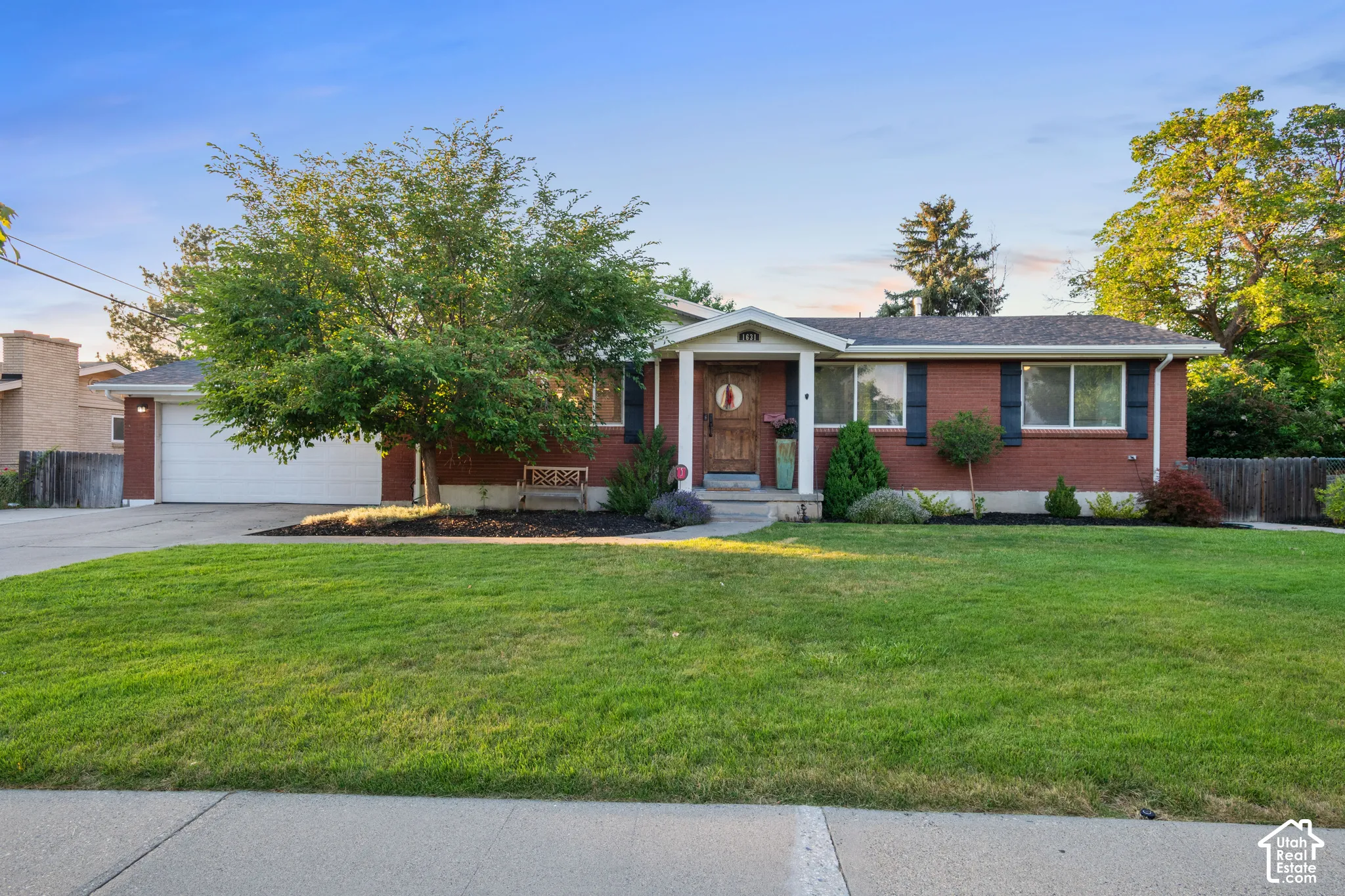 Brick exterior with a covered entry with white columns, attached garage, concrete driveway, and a landscaped front yard