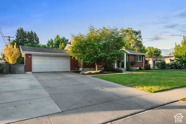 Brick exterior featuring a two-car garage, concrete driveway, and a manicured lawn