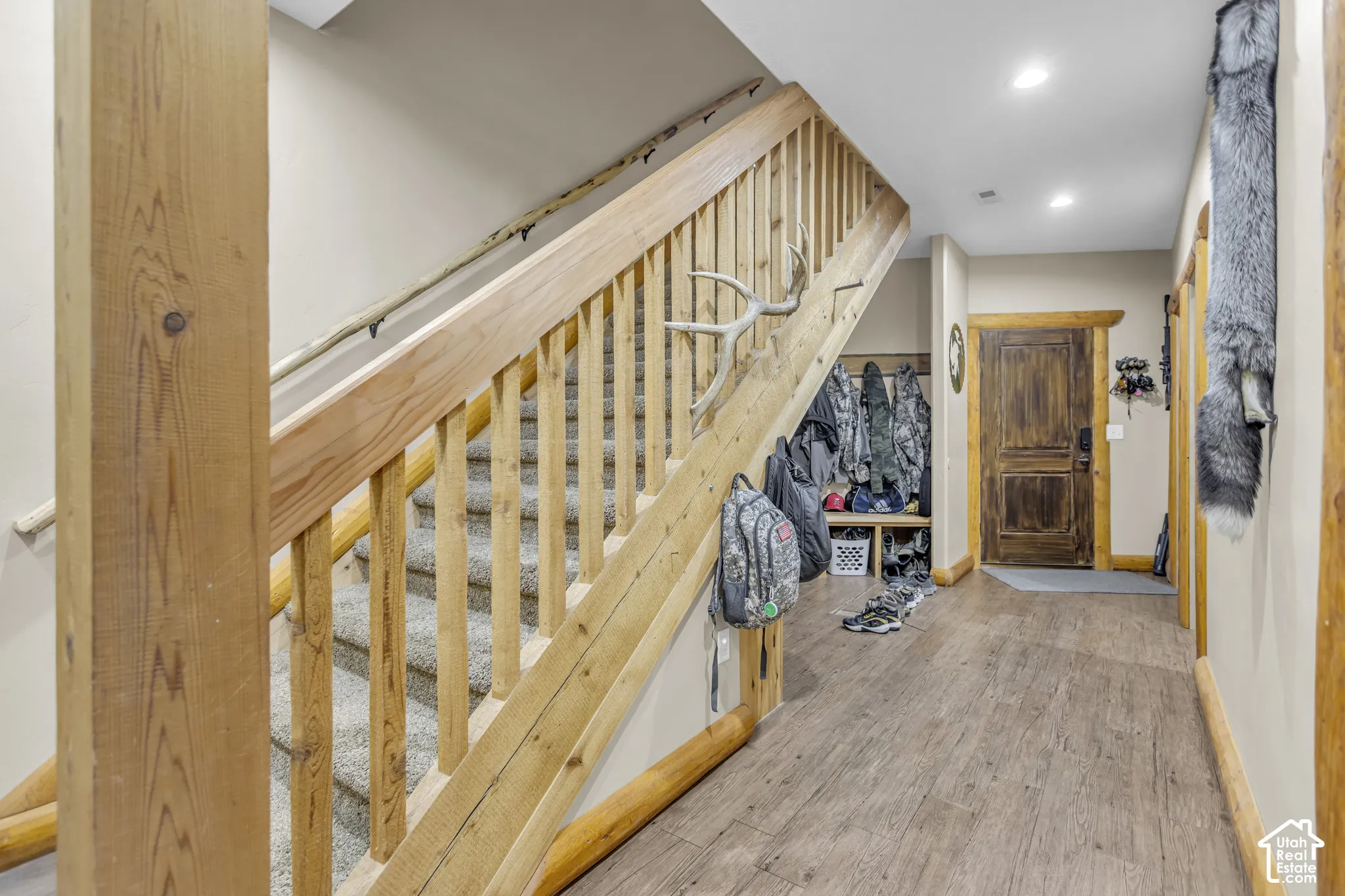 Wood-finish flooring, recessed lighting, wood staircase with carpeted treads, and wood-paneled door with wood trim