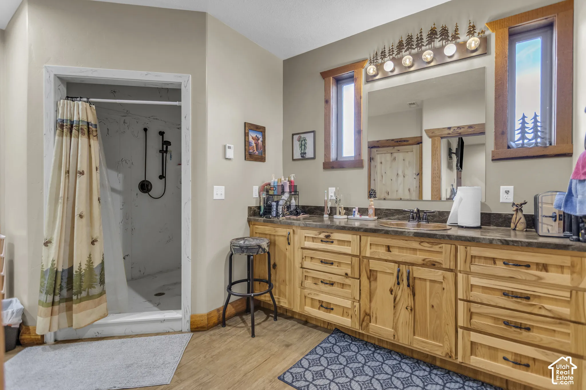 Wood-finish flooring with a multi-drawer vanity featuring natural wood cabinetry, a dark countertop, and dual sinks