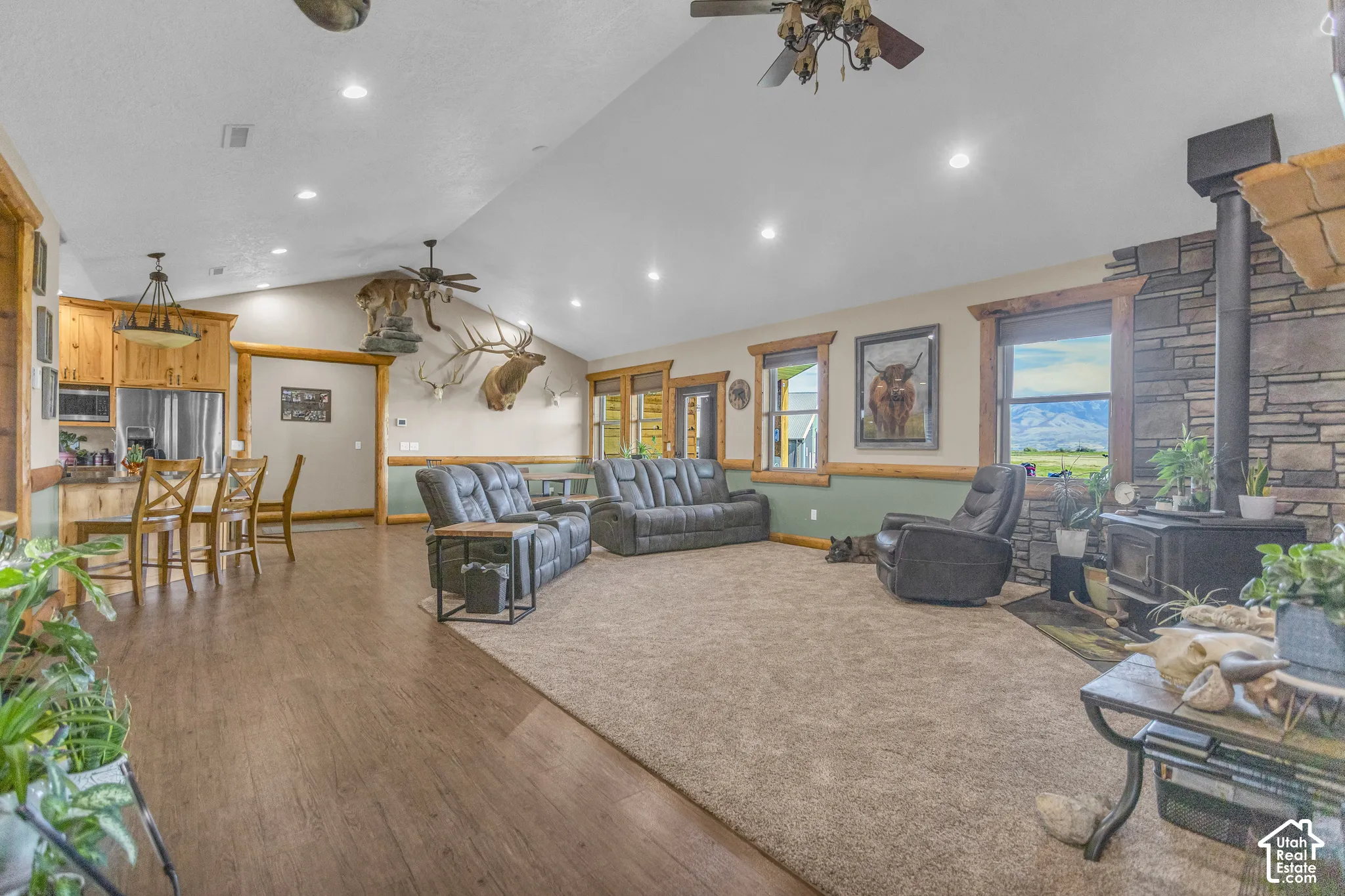 Vaulted ceiling with recessed lighting, wood-finish flooring, stone-clad wood-burning stove, wood trim windows, and built-in wood cabinetry