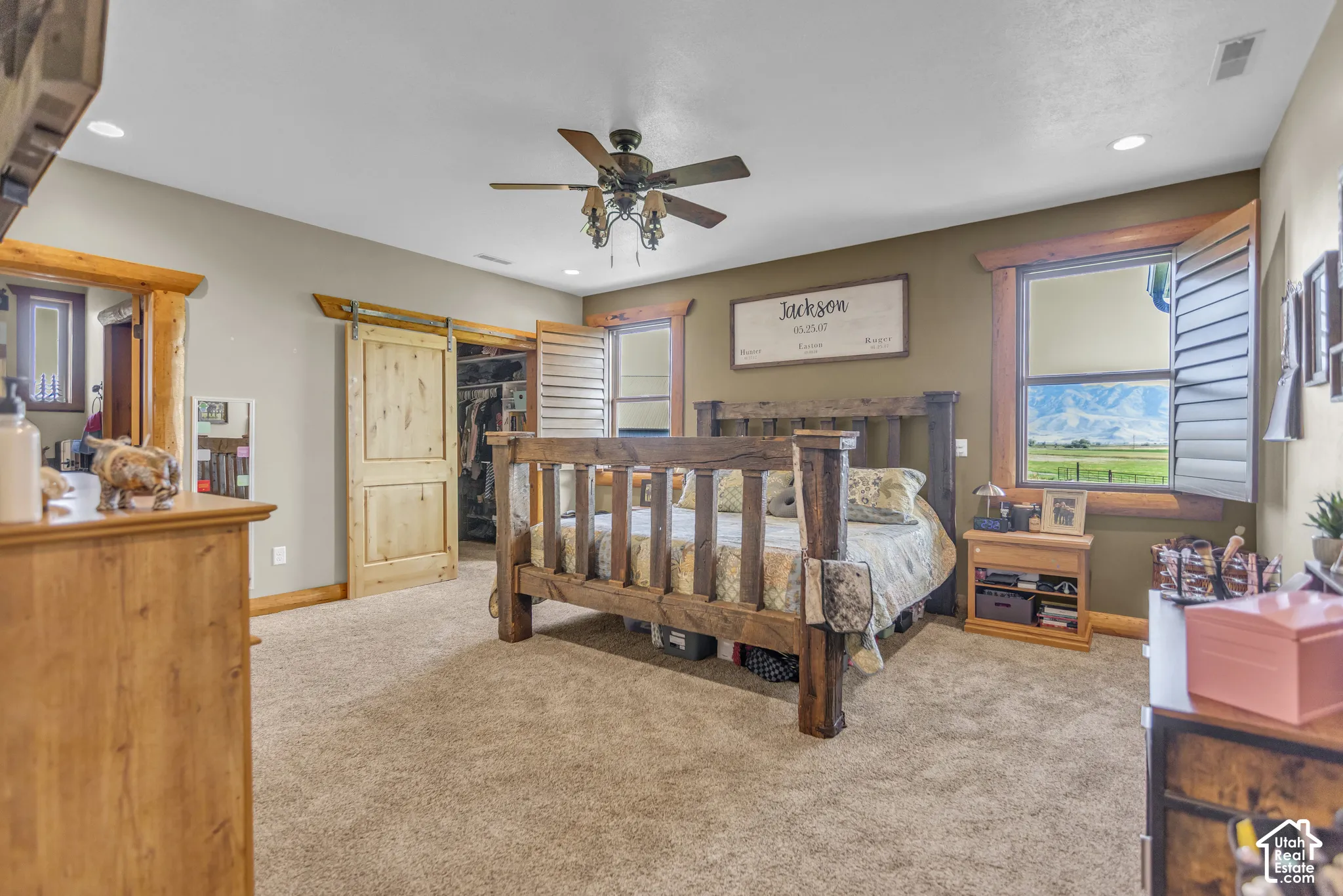 Carpeted flooring, recessed lighting, ceiling fan, wood-finish barn door, and a window with mountain scenery