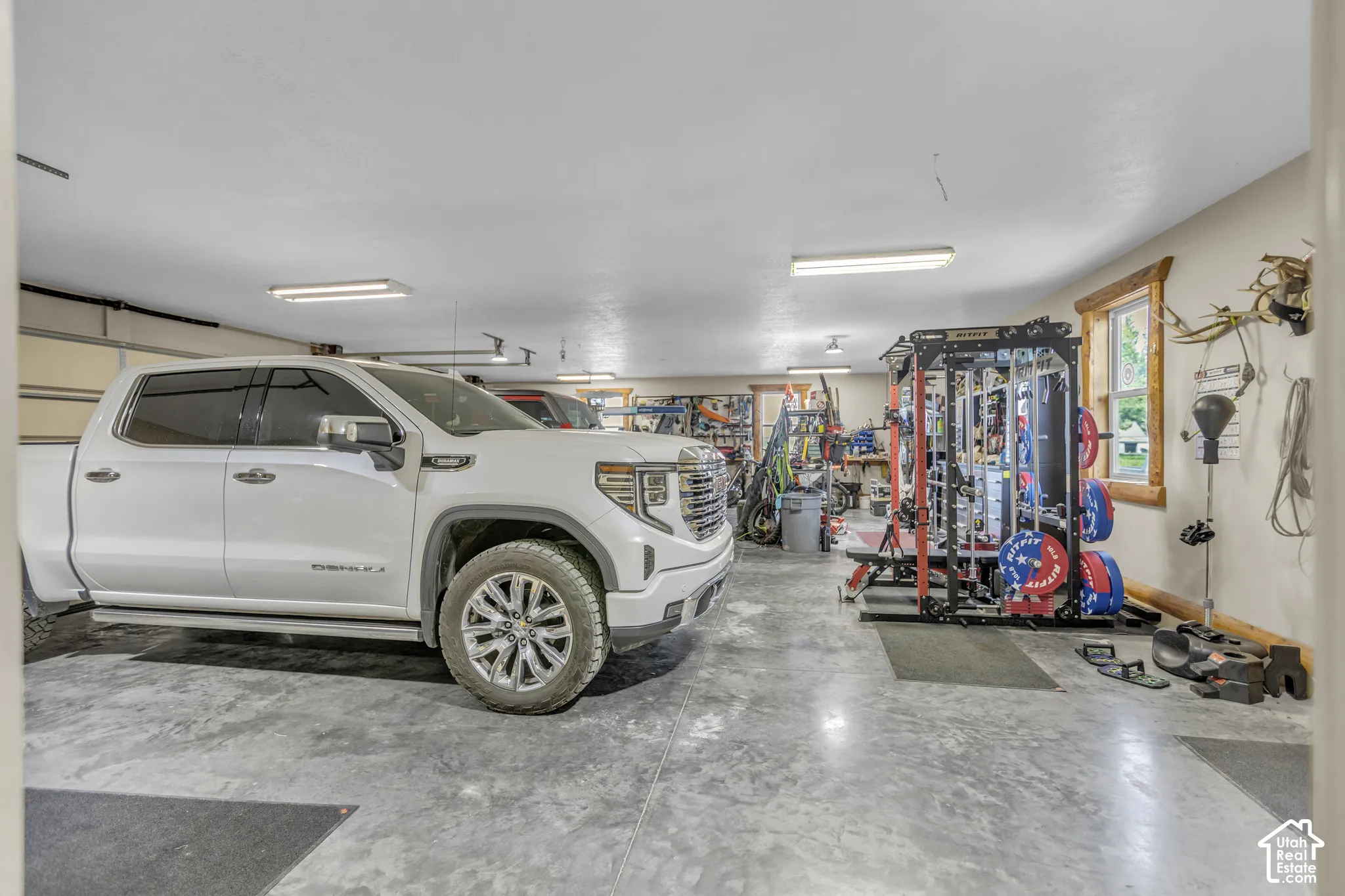 Spacious garage with durable concrete flooring, multiple overhead lighting fixtures, and a window with wood trim