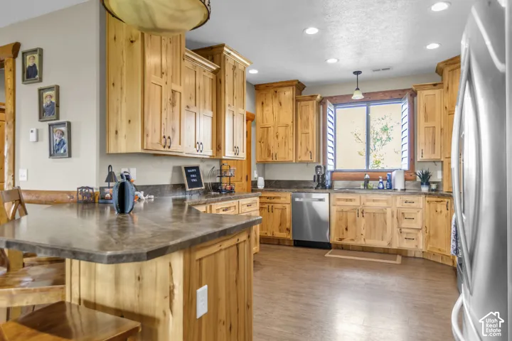 Kitchen featuring light wood cabinetry, stone-finish countertops, stainless steel appliances, and wood-finish flooring
