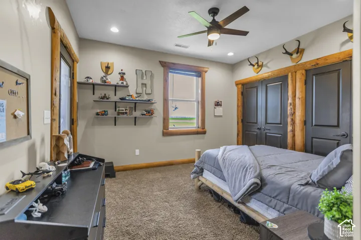 Plush carpet flooring, integrated recessed lighting, ceiling fan, and window with wood-finish trim