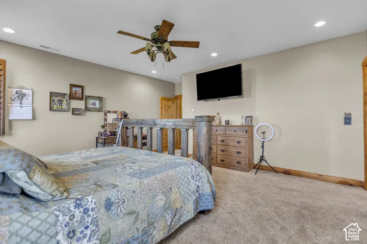 Recessed lighting, wood-finish ceiling fan, mounted television, wood-finish structural beams, and carpet flooring