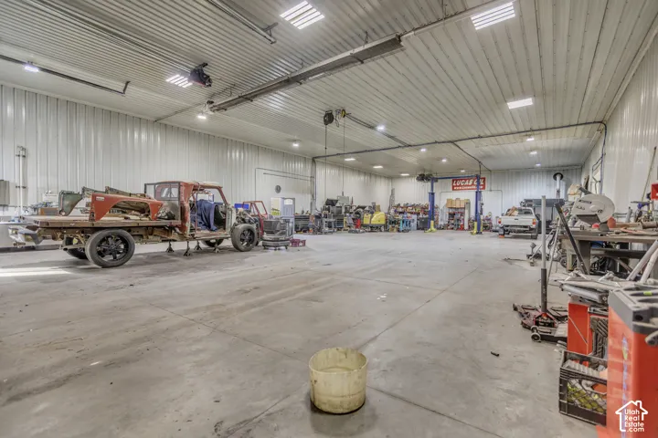 Spacious workshop with concrete flooring, high ceilings, bright overhead lighting, and white corrugated metal walls