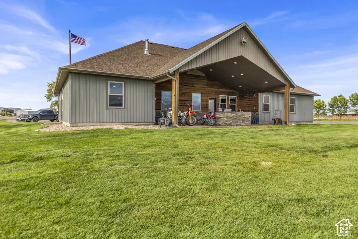 Expansive green lawn, covered outdoor patio, stone-clad outdoor kitchen, vertical siding, and a gabled roofline