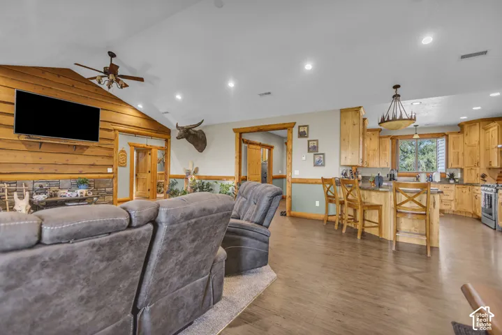 Vaulted ceiling with wood-finish flooring, wood-paneled accent wall, stone-front fireplace, and recessed lighting