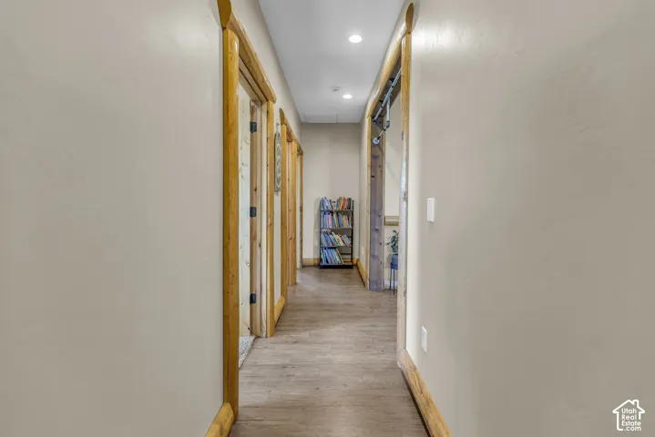 Hallway featuring recessed lighting, wood-finish flooring, and natural wood trim around doorways