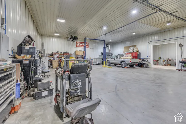Large open garage space with concrete flooring, high ceilings, ample lighting, and a vehicle lift