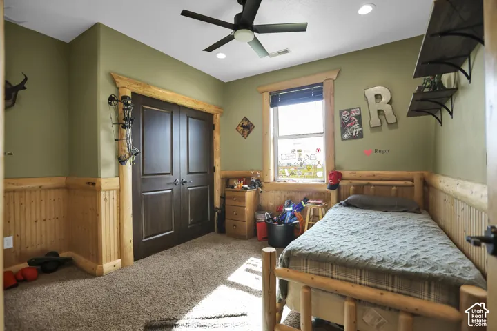 Wall-to-wall carpeting, wood-paneled wainscoting, and a ceiling fan with integrated lighting