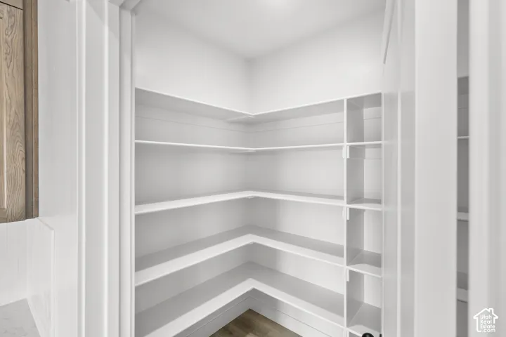 Spacious pantry featuring extensive shelving, white finishes, and wood-finish flooring