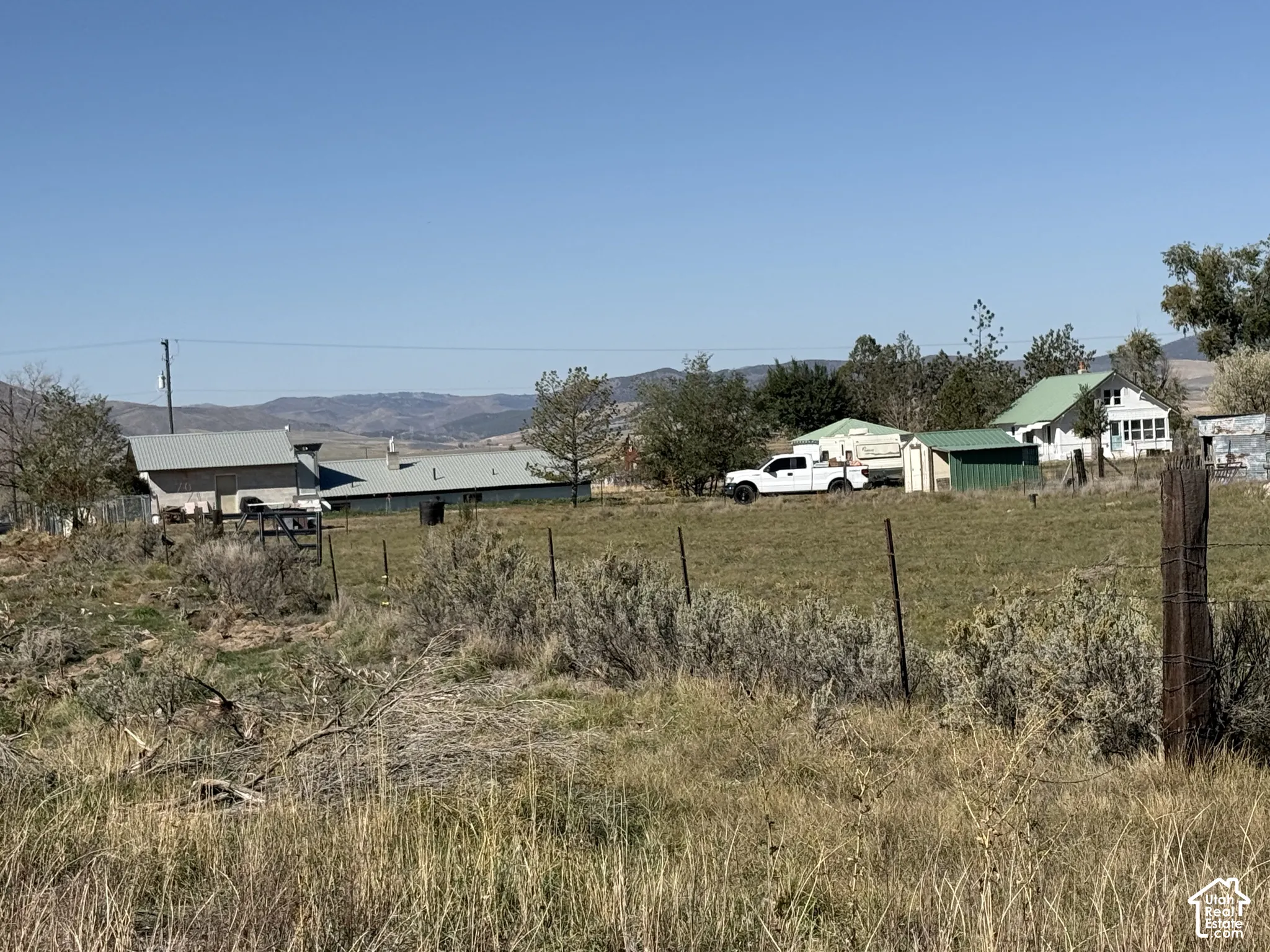 Expansive rural property featuring a large open field, distant mountain scenery, and multiple structures