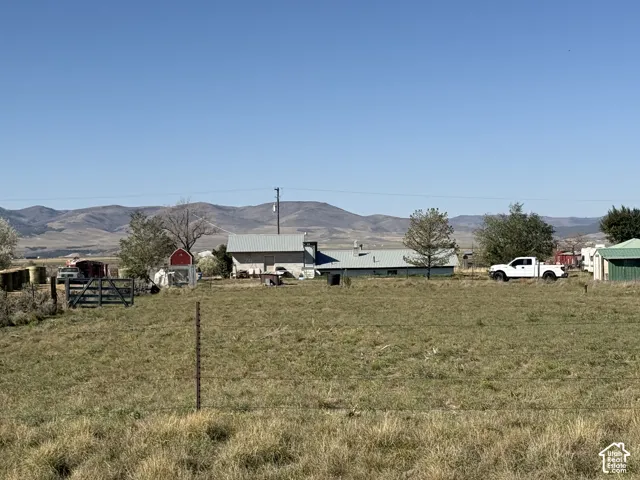 Expansive grassy landscape with distant mountain scenery, featuring a property with multiple structures and a clear sky