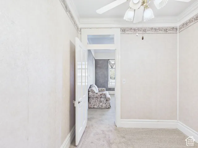 Carpeted room with crown molding, decorative wallpaper border, and a ceiling fan with integrated lighting
