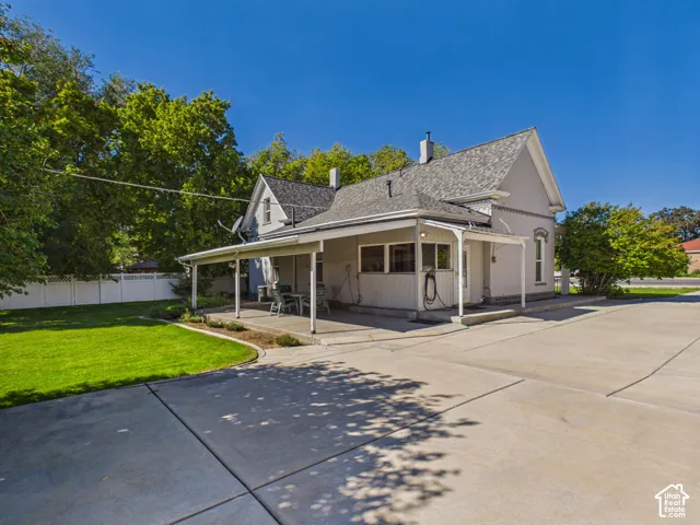 Exterior featuring a covered patio, expansive paved driveway, and manicured lawn with mature trees