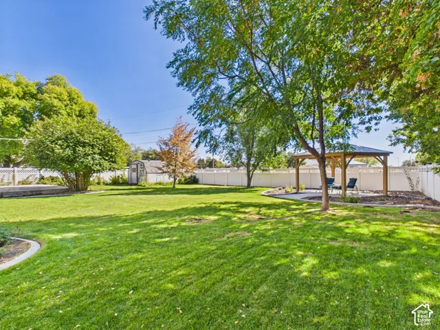 Expansive lawn area, mature trees, white perimeter fencing, wood-framed gazebo with a dark roof, and a concrete patio