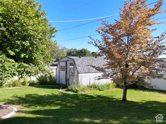 Expansive green lawn with mature trees and a storage shed featuring an asphalt shingle roof