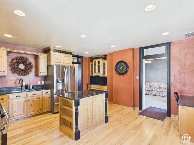 Recessed lighting, wood-finish flooring, light wood cabinetry, dark countertops, and a kitchen island