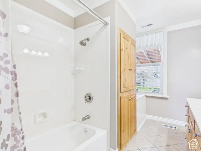White tub and shower combination with chrome fixtures, wood-finish built-in cabinetry, tiled flooring, and a large window with blinds