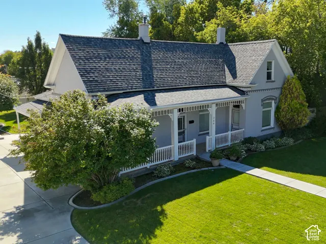 Gable-roof property featuring a covered front porch with white railing, mature landscaping, paved driveway, and established front lawn