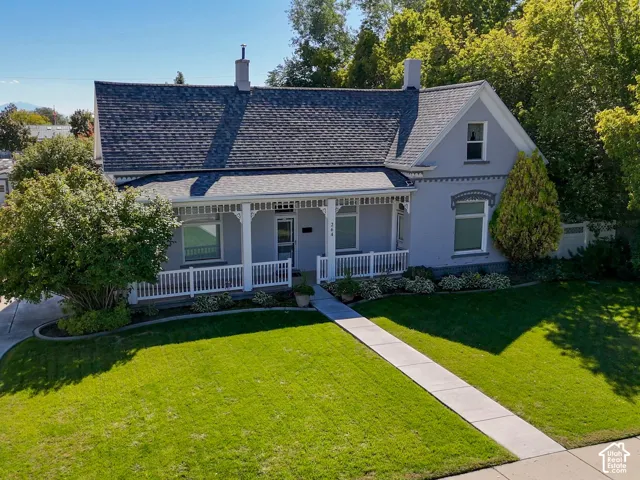 Charming exterior featuring a covered front porch, a well-maintained lawn, mature trees, and a concrete pathway