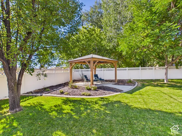 Expansive lawn area with mature trees, a white perimeter fence with lattice detailing, and a freestanding gazebo on a concrete pad