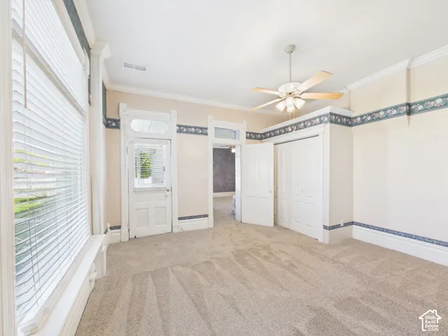 Carpeted interior with crown molding, a ceiling fan, and white trim