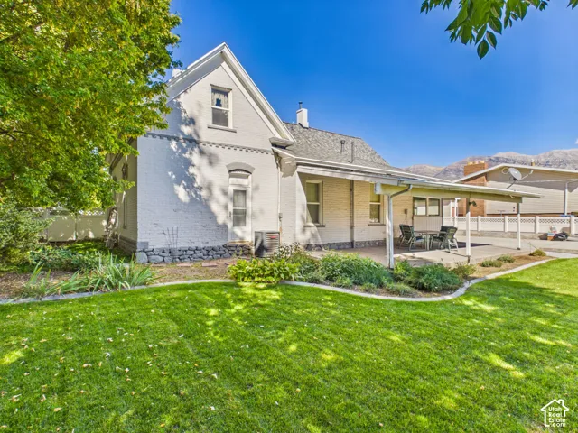 White brick exterior with a pitched roof, a covered patio, and a manicured lawn
