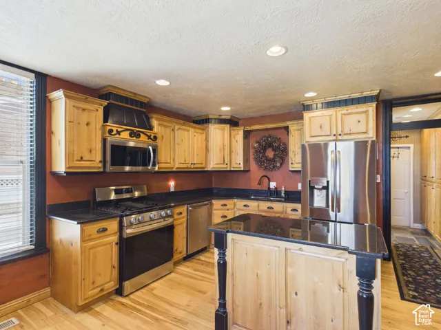 Kitchen featuring wood-finish cabinetry, dark countertops, stainless steel appliances, and a central island