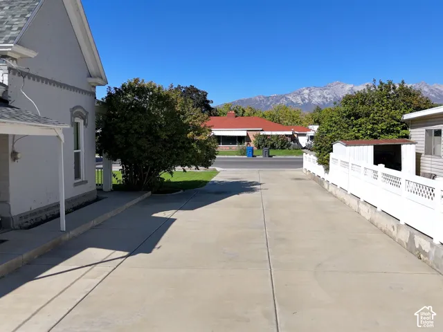Expansive concrete driveway, white lattice fence, mature landscaping, and mountain scenery