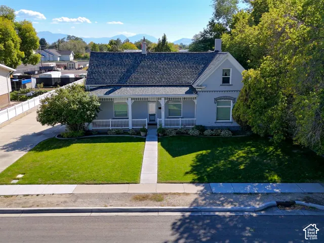 Light gray exterior with white trim, covered front porch, asphalt shingle roof, and a mature front yard tree