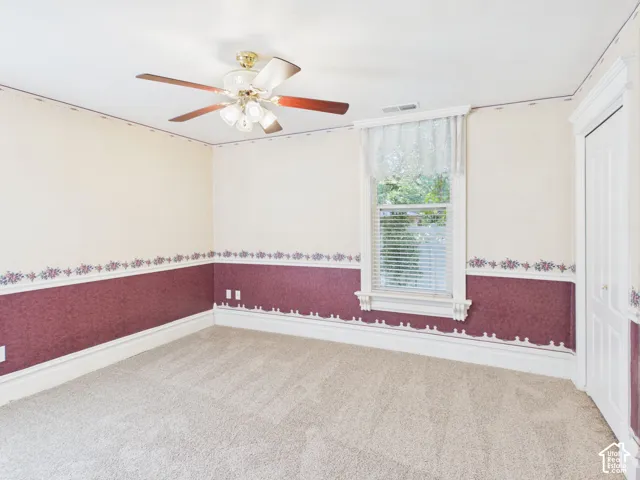 Neutral-toned carpeting, ceiling fan with light fixture, window with blinds, and white trim details