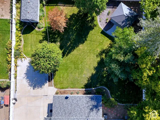 Expansive backyard featuring a manicured lawn, mature trees, a detached outbuilding, and a covered patio structure
