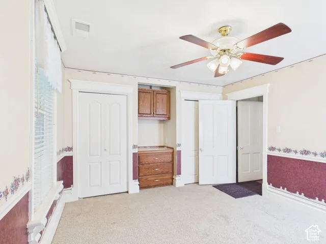 Light-colored carpeting, white interior doors, built-in wooden cabinetry, and a ceiling fan with integrated lighting
