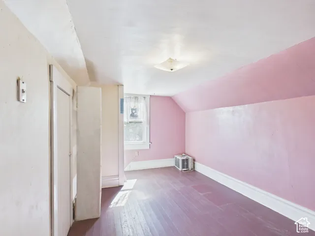 Sloped ceiling with an attached light fixture, a window with trim, wood-finish flooring, and painted walls