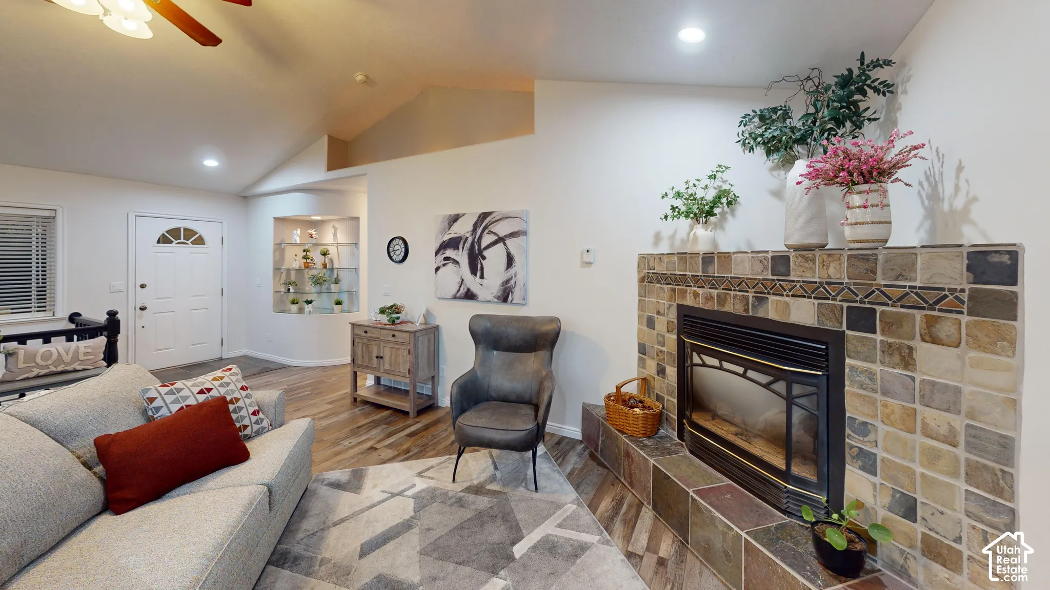 Living area with vaulted ceiling, wood-finish flooring, built-in fireplace with stone tile surround, recessed lighting, and a front entry door with an arched window insert